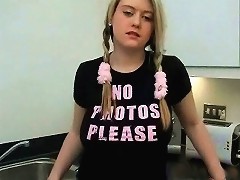 A young, blonde girl is standing in the kitchen corner. The cameraman asks her to lift her T-shirt so he can film her large