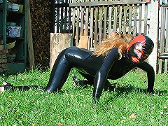 Blonde Marketa in black latex suite sits in her garden like a wild cat ready to atack!