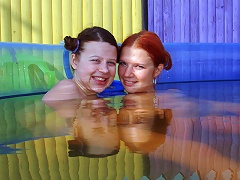 Two teenage girls are playing around in a small swimming pool outdoors. They lick at a couple of dildos and then conti