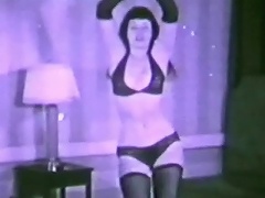 A girl in a black bikini and black stockings is dancing around in front of the camera, swaying her ass and her tits about.